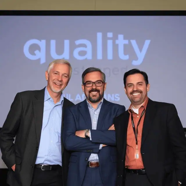 Three quality managers in suits standing next to each other smiling