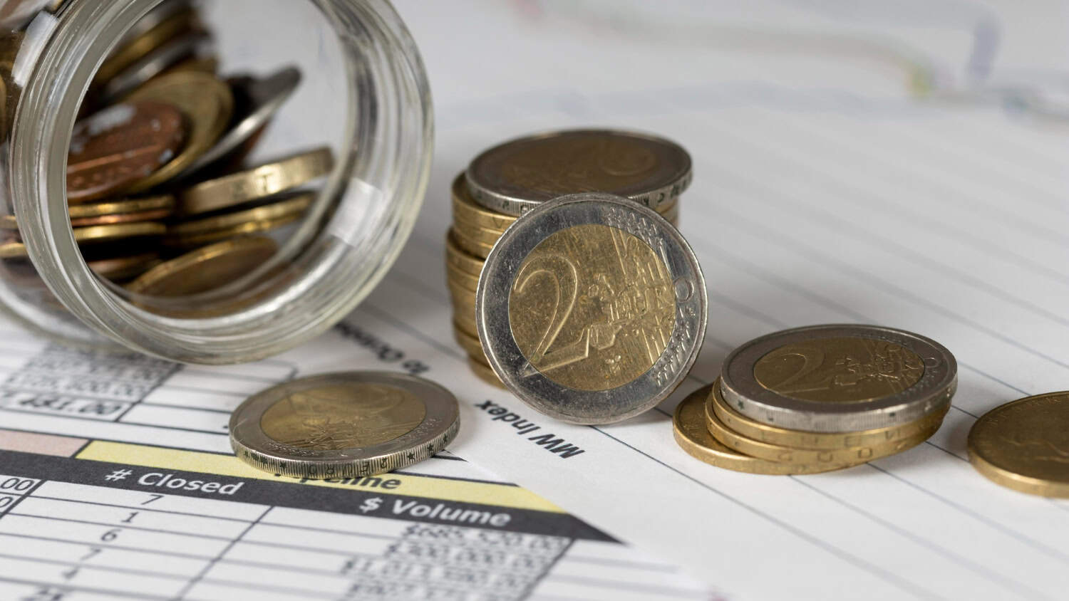 Euro coins spilling out of a jar on piece of paper