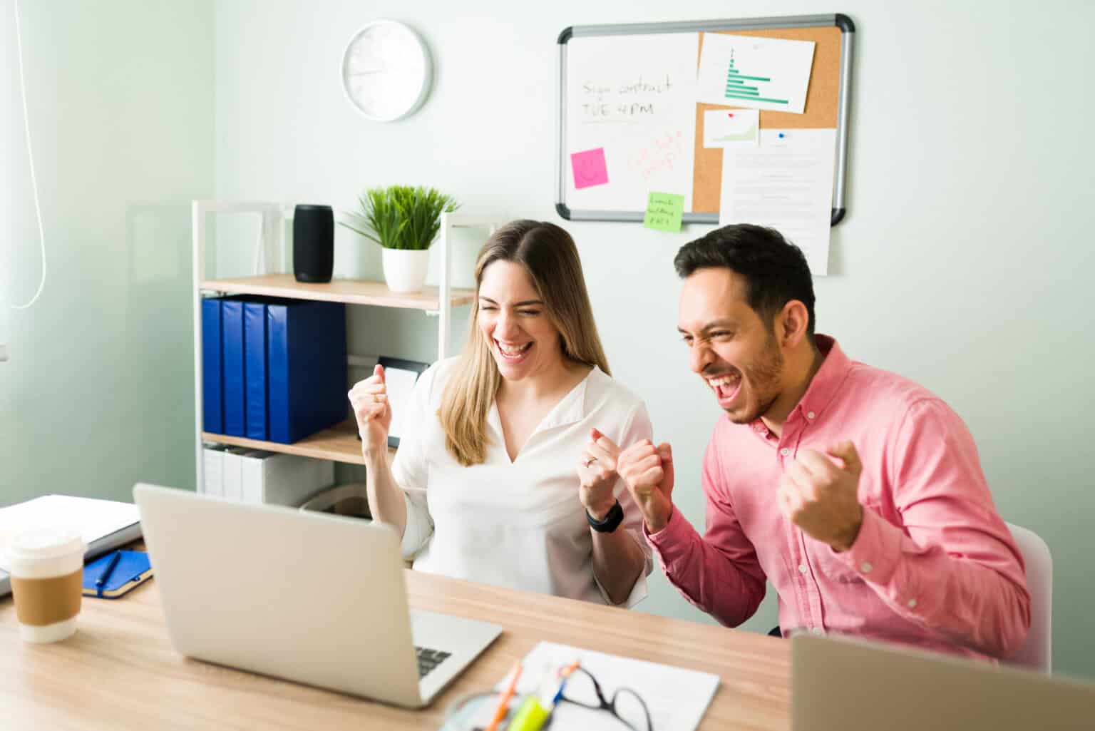 Excited colleagues cheering during an online meeting at the office, celebrating after making a work deal on a video call on their laptop