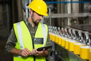 Male worker using digital tablet in juice factory to do quality control of products