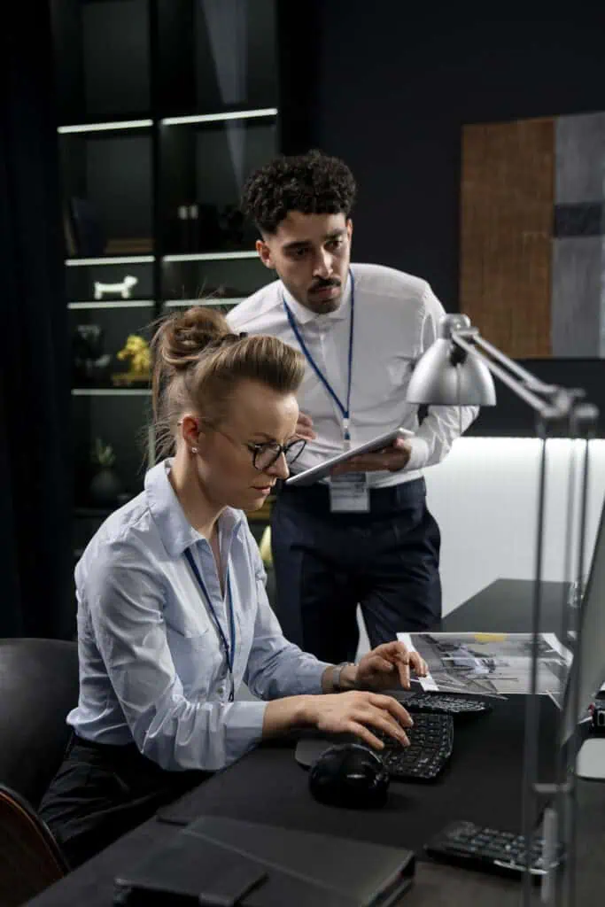 Two system integration engineers working together, woman is sitting in front of computer, man leaning in to see