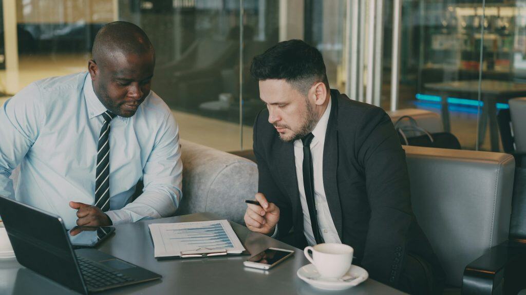 Two men sit in office, leaning over a paper report