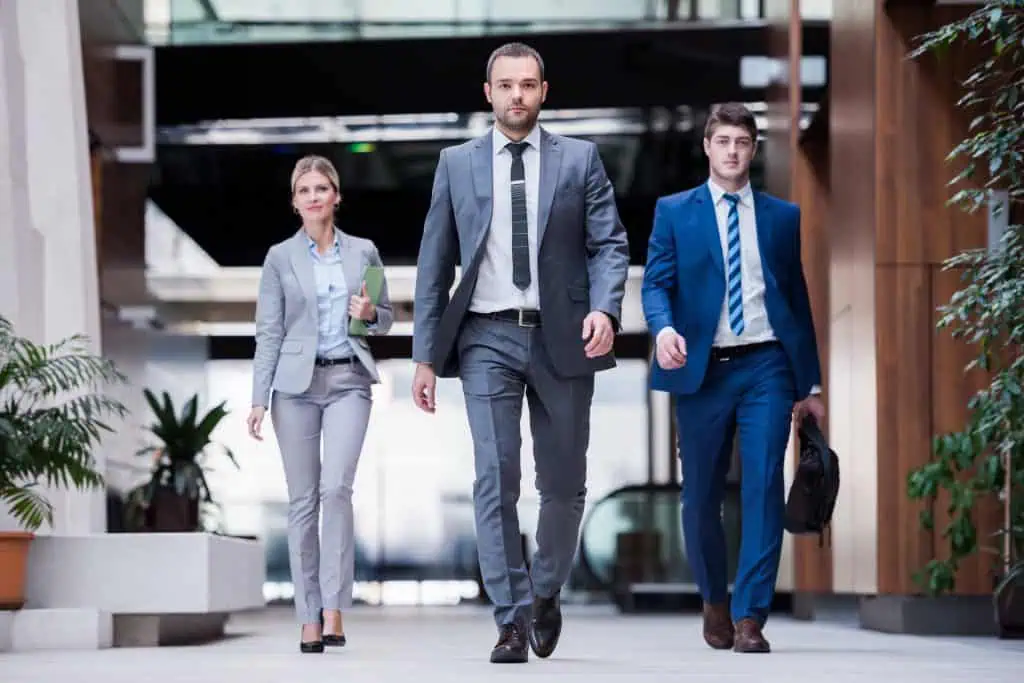 Three team leaders dressed in suits, two men and one woman, confidently walk through office hallway