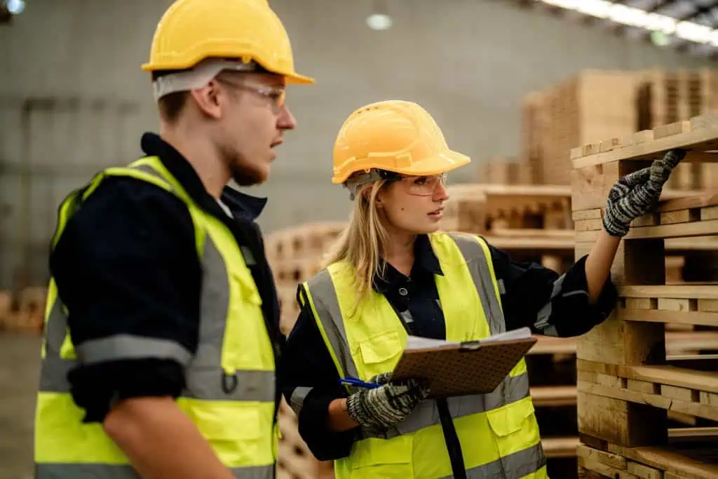 Warehouse workers, man and woman, wearing protective gear are inspecting timbers wood in warehouse