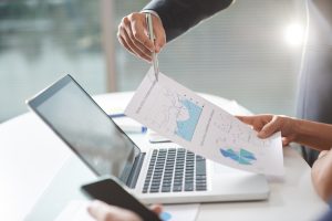 Two coworkers in modern company office are using paper graphs and laptop