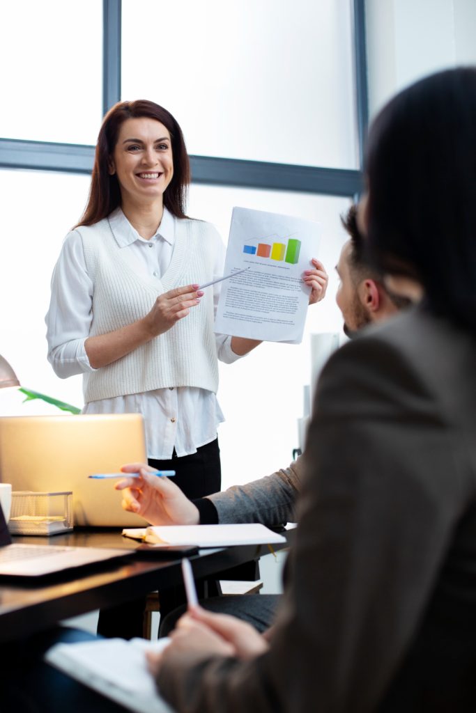 A product leadership expert standing in office with a paper graphs in her hands, pointing out numbers to her team
